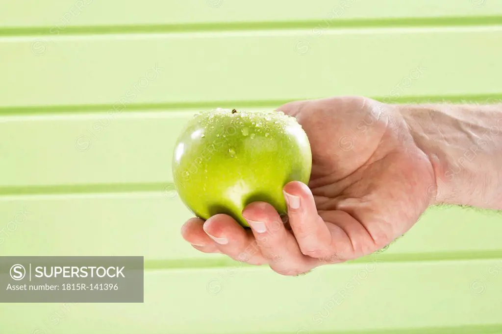 Mature man holding granny smith against green background, close up