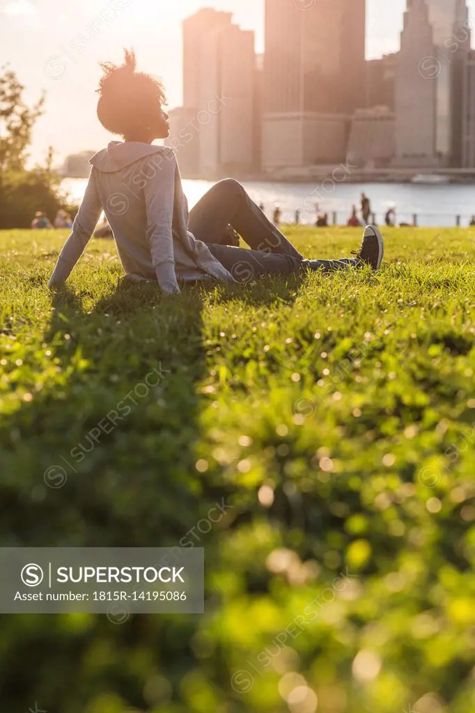 USA, New York City, Brooklyn, woman sitting on meadow looking at the skyline