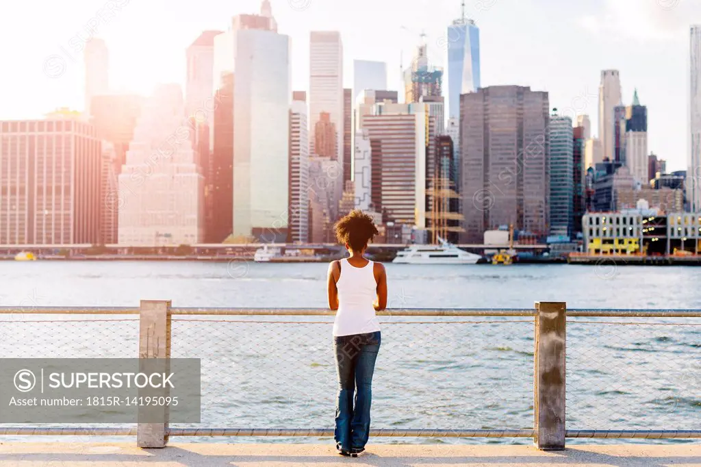 USA, New York City, Brooklyn, woman standing at the waterfront looking at the skyline