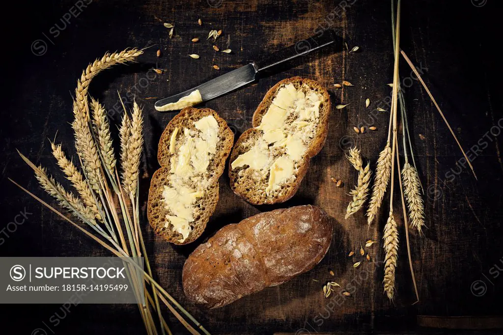Buttered bread and ear of wheat on dark wood