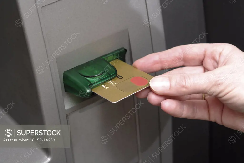 Hand pushing credit card into cash terminal, close-up