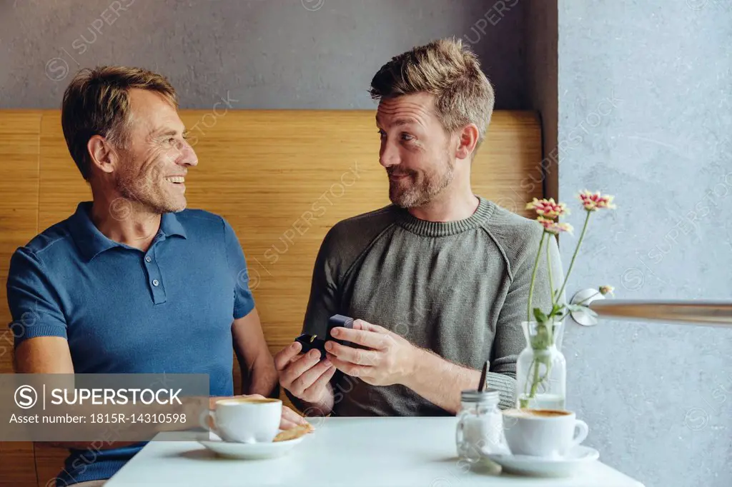 Gay man offering wedding ring to partner in cafe