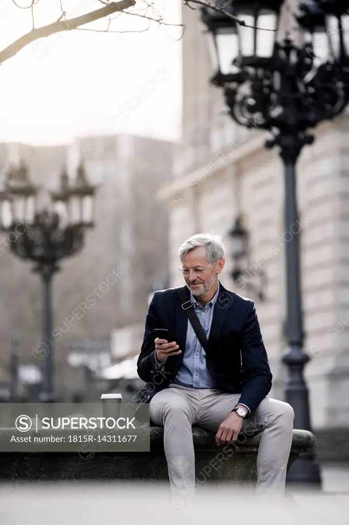 Grey-haired businessman in the city with smartphone and coffee to go