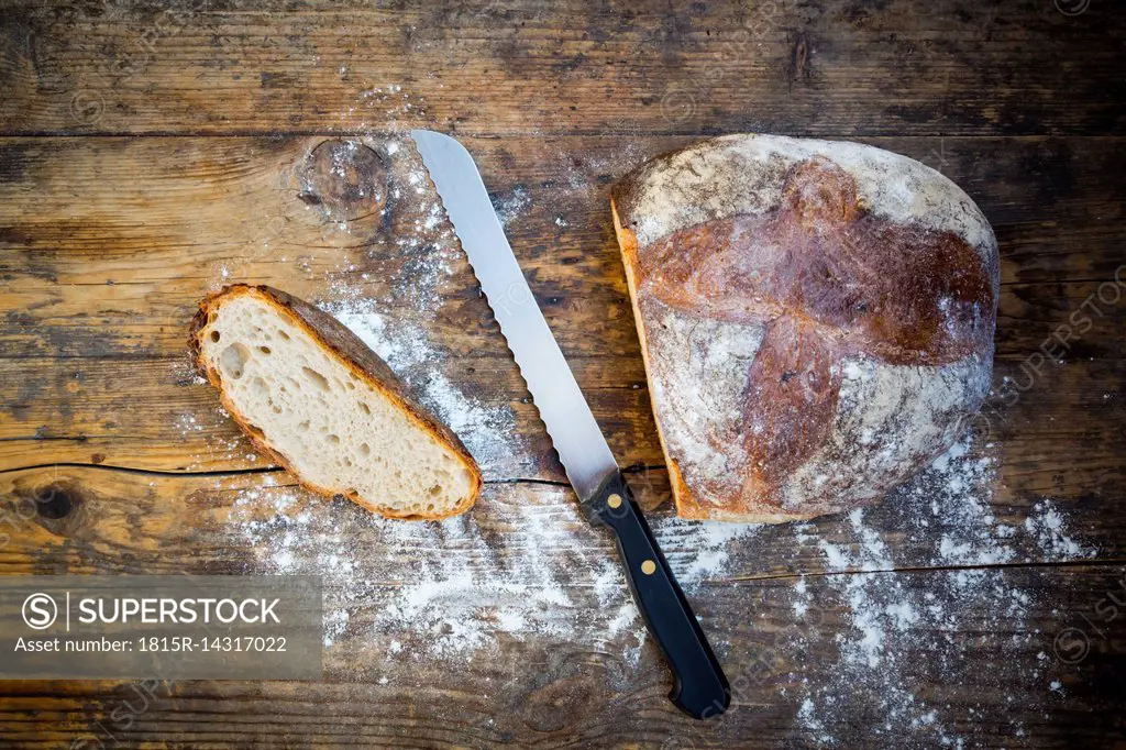Cut wheat bread powdered with flour and bread knife on dark wood