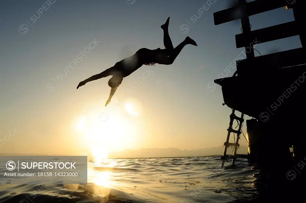 Man jumping fom jetty into the sea at sunset