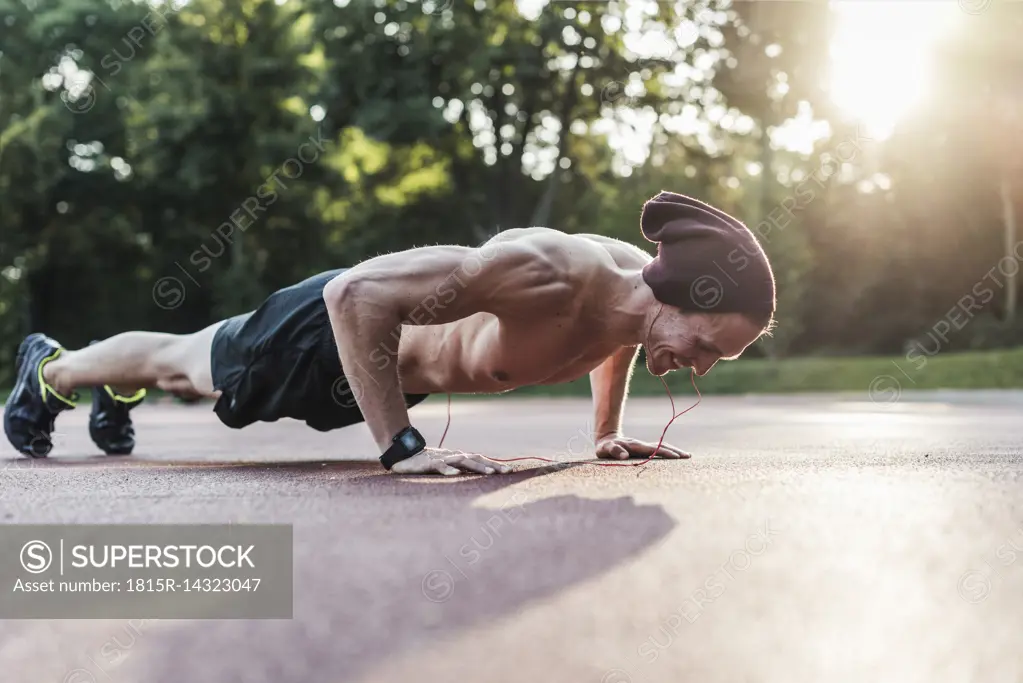 Shirtless man exercing push ups on sport field