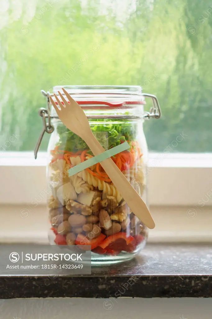 Preserving jar of vegan mixed salad with tofu and pasta on window sill
