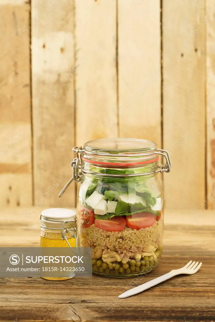 Preserving jar of mixed salad with peas, tuna, couscous, tomatoes, tuna, feta and jar of vinaigrette dressing