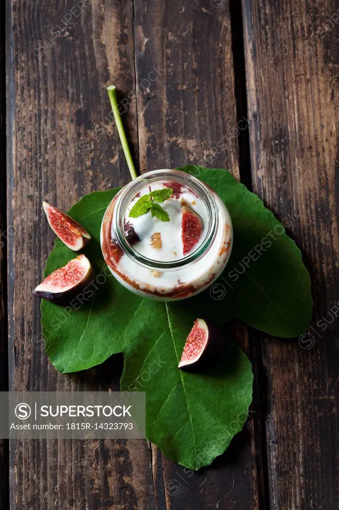 Glass of Mascarpone cream with fig compote and walnuts on fig leaf and dark wood