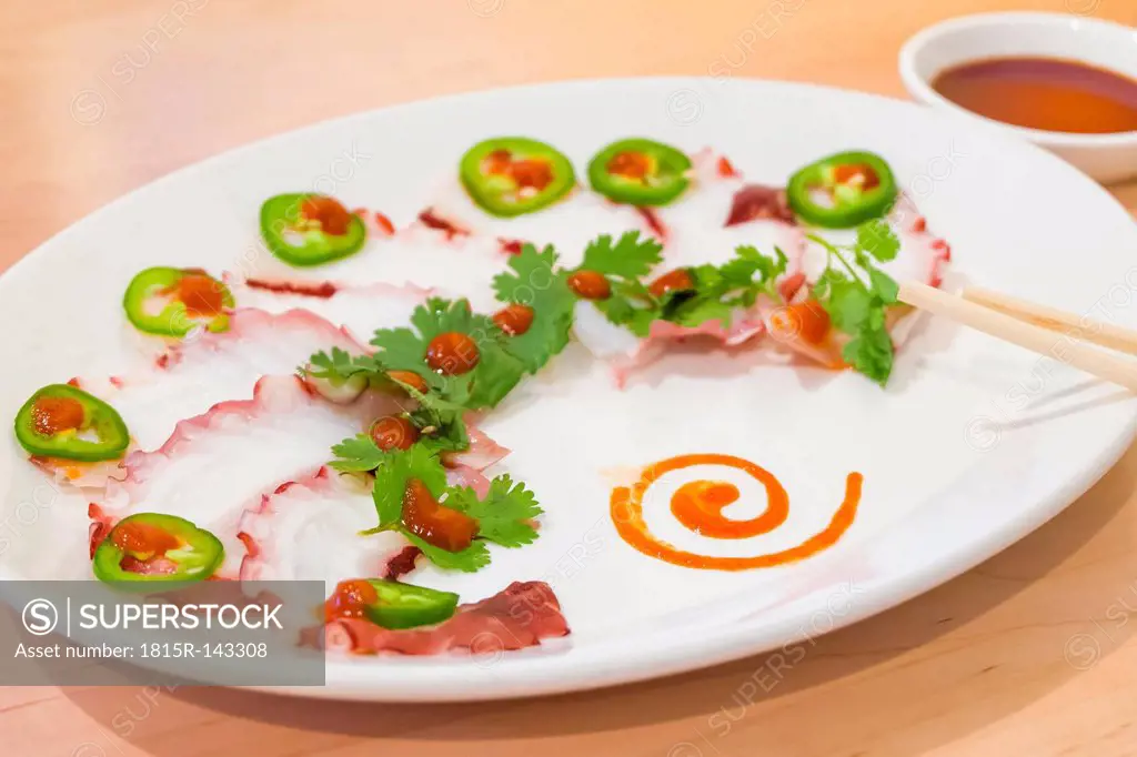 Plate of Japansese sashimi slices garnished with coriander and jalapenos