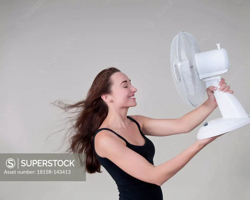 Young woman with electric fan, smiling