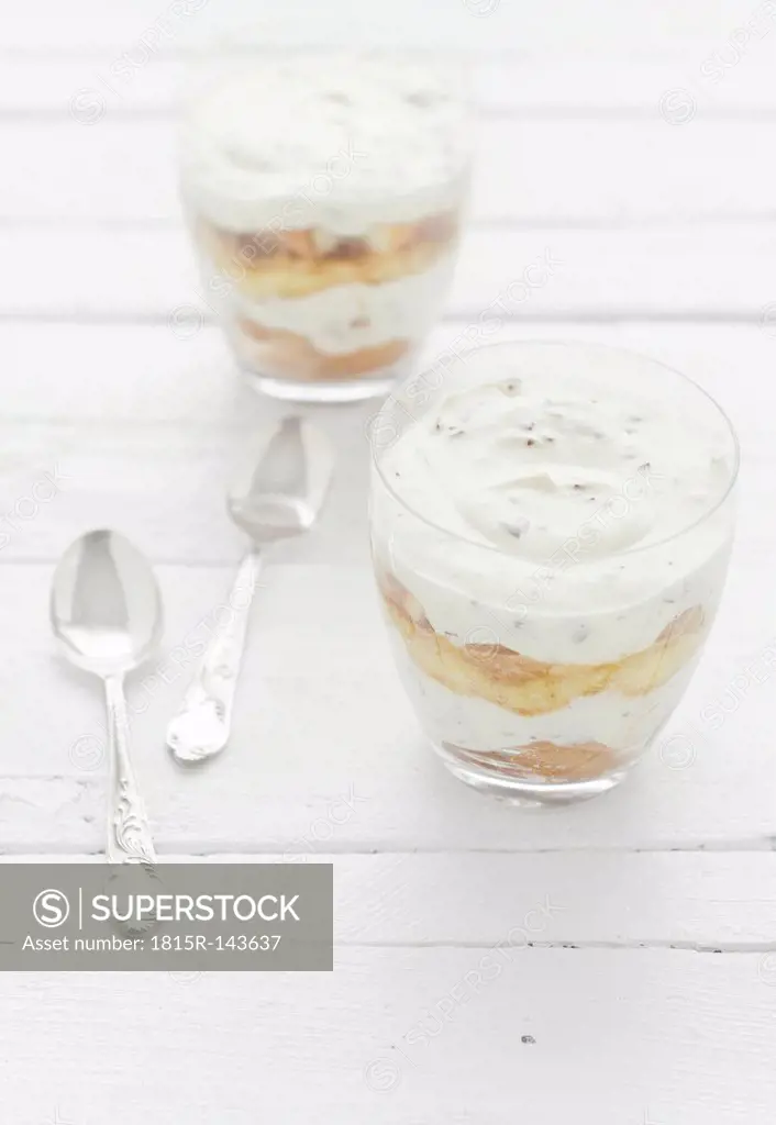 Two glasses of marshmallow, tiramisu, chocolate and banana flavour with spoon on wooden table, close up