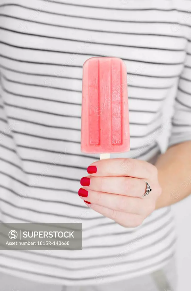 Studio, young woman with red nail polish holding a red popsicle