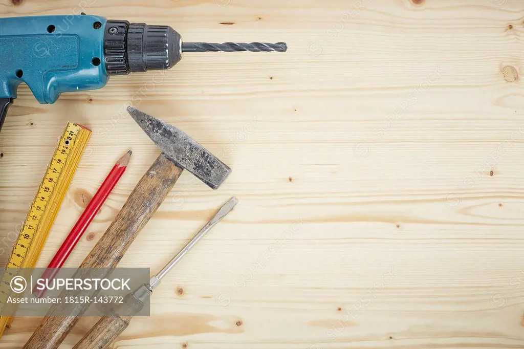 Drill, pencil, hammer, screwdriver, folding ruler on wood, close up