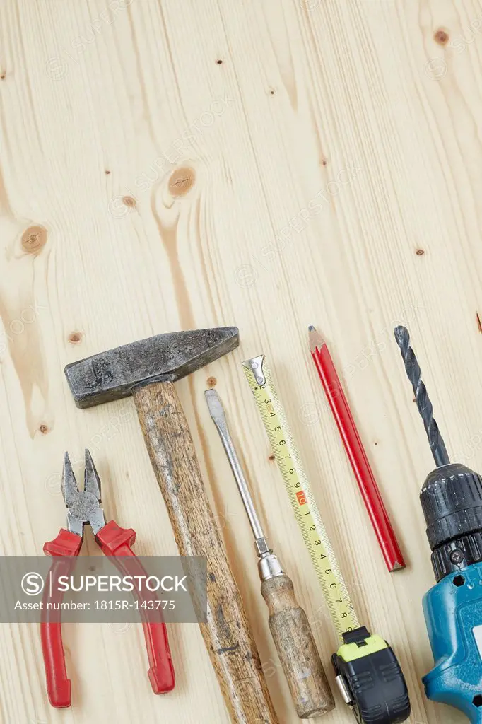 Hammer, screwdriver, pencil, drill, measuring tape, hammer, plier on wood, close up