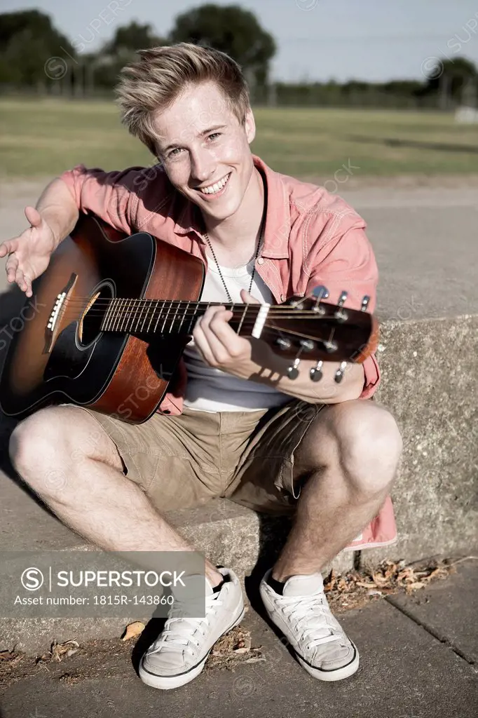 Germany, Young man playing guitar in park