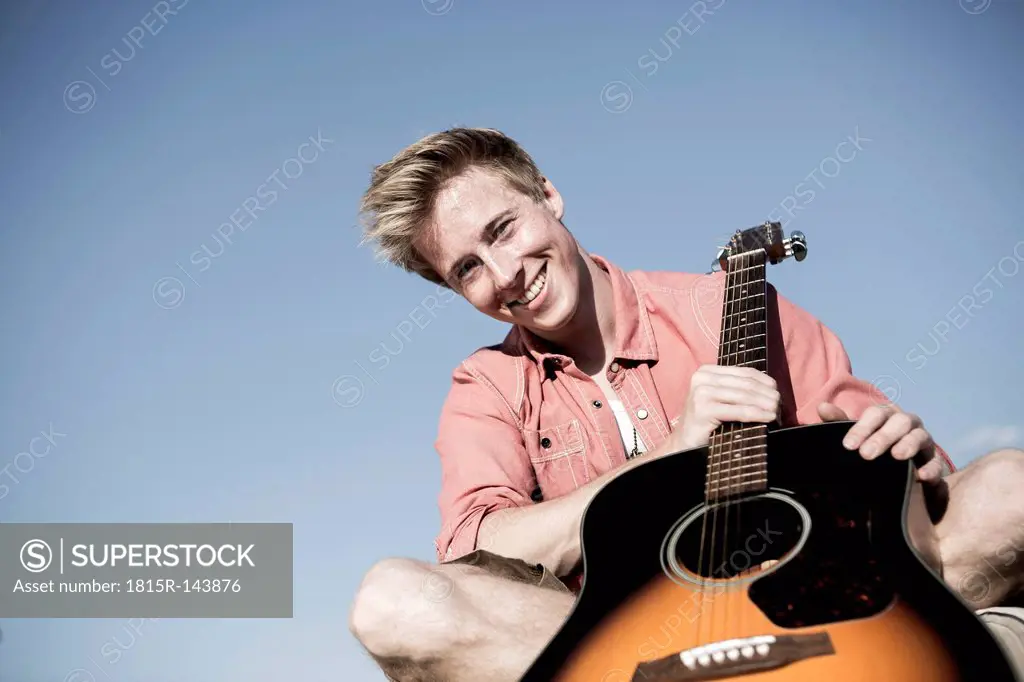 Germany, Young man holding guitar, smiling