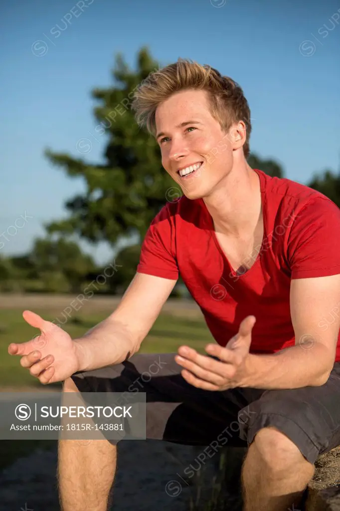 Germany, Young man sitting in park, gesturing