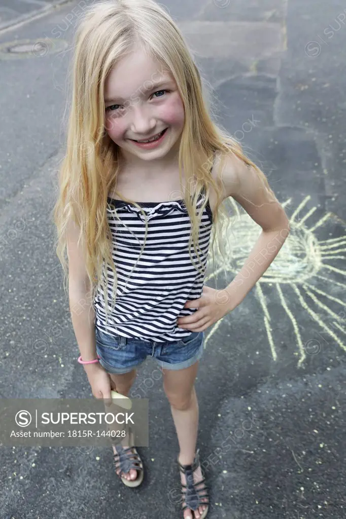Germany, North Rhine Westphalia, Cologne, Portrait of girl drawing sun on street, smiling, close up