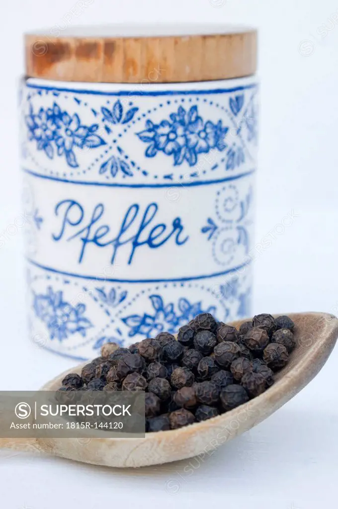 Peppercorns on wooden spoon with jar on white background, close up