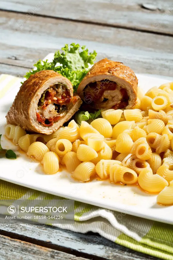 Plate of pork roulades and pasta on wooden table, close up