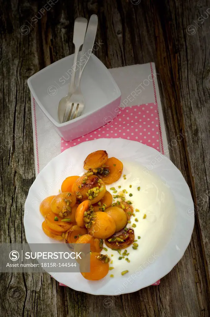 Caramelized apricots with yoghurt and pistachios on wooden table, close up