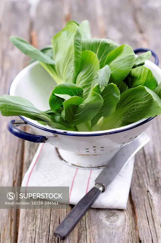 Green pak choi with colander and knife, napkin on wooden table, close up