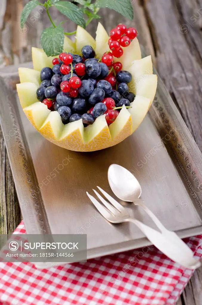 Honeydew melon with red currant and blueberries, tray on wooden table, close up