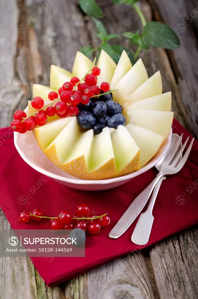Bowl of honeydew melon with red currant and blueberries on wooden table, close up