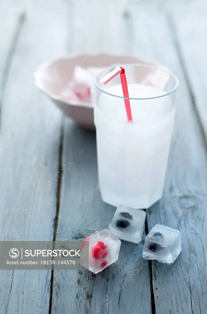 Glass of soda with ice cubes and frozen berries on wooden table, close up