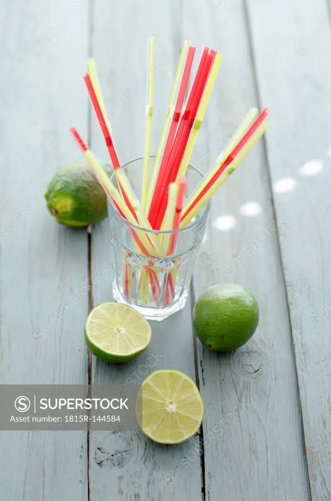 Glass with straws and limes on wooden table, close up