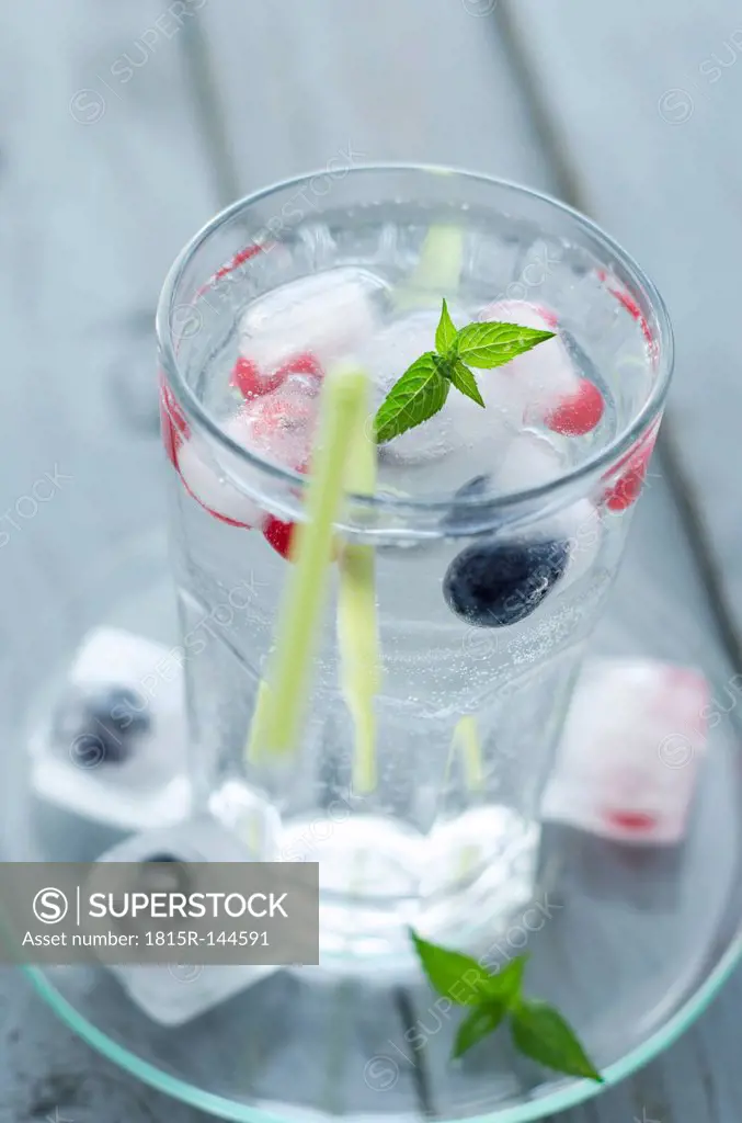 Glass of mineral water with ice cubes and frozen berries on wooden table, close up