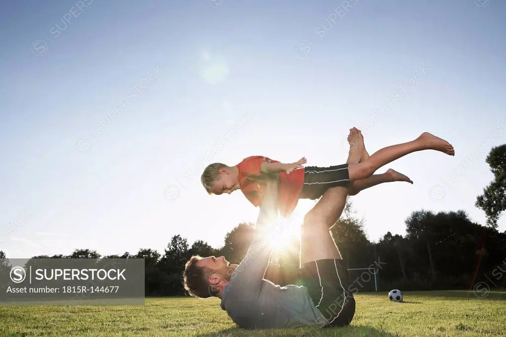 Germany, Cologne, Father holding son aloft on soccer field