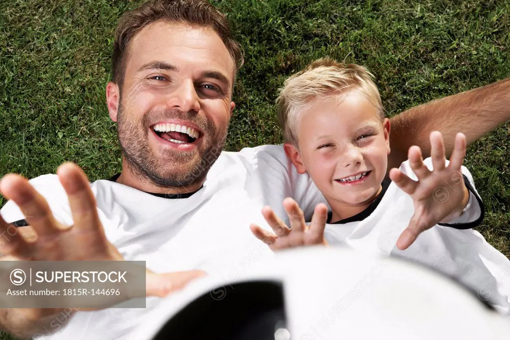 Germany, Father and son lying on lawn, wearing football shirts