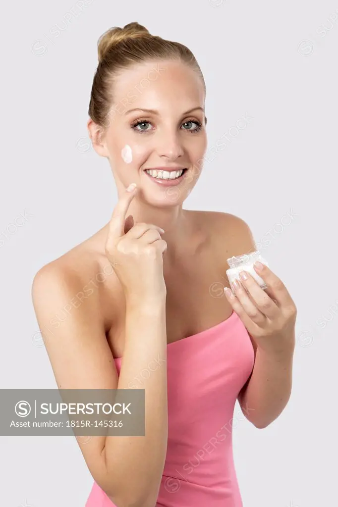 Portrait of young woman applying cream on face, smiling