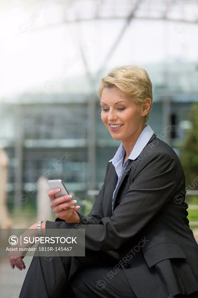 Germany, Hannover, Businesswoman using smart phone, smiling