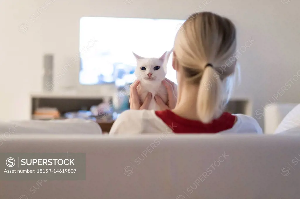 Woman sitting with her cat on the couch watching TV