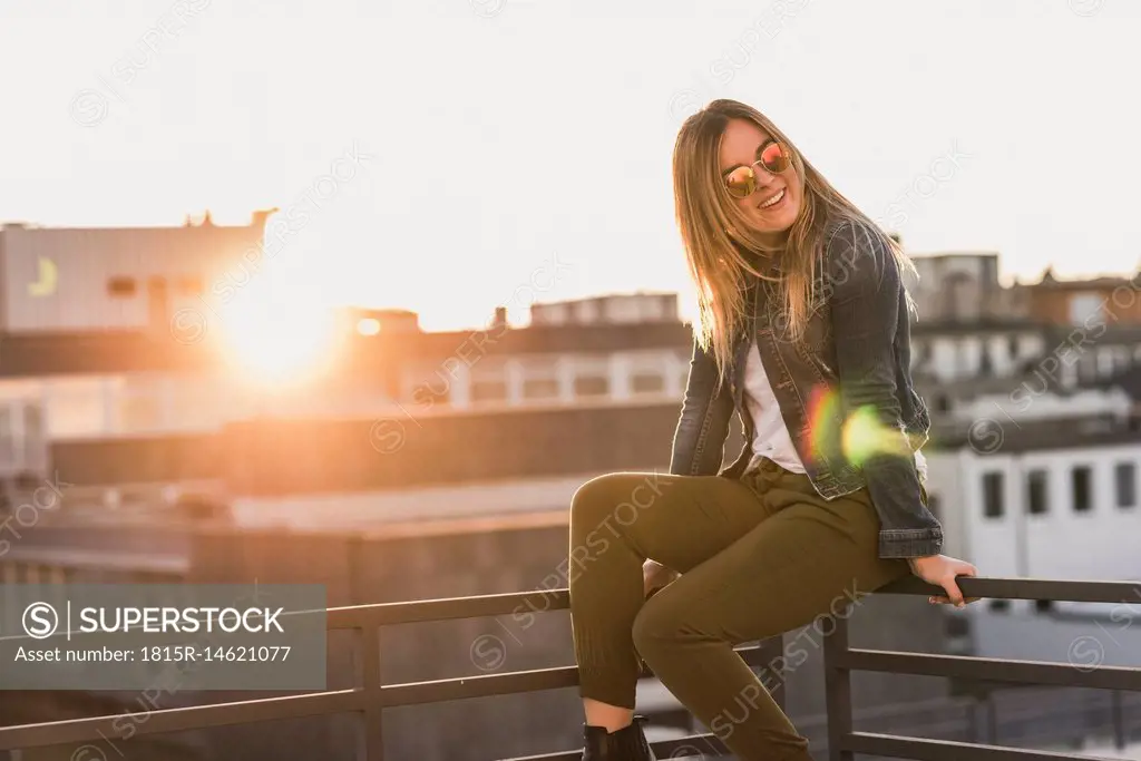 Young woman sitting on railing in the city at sunset
