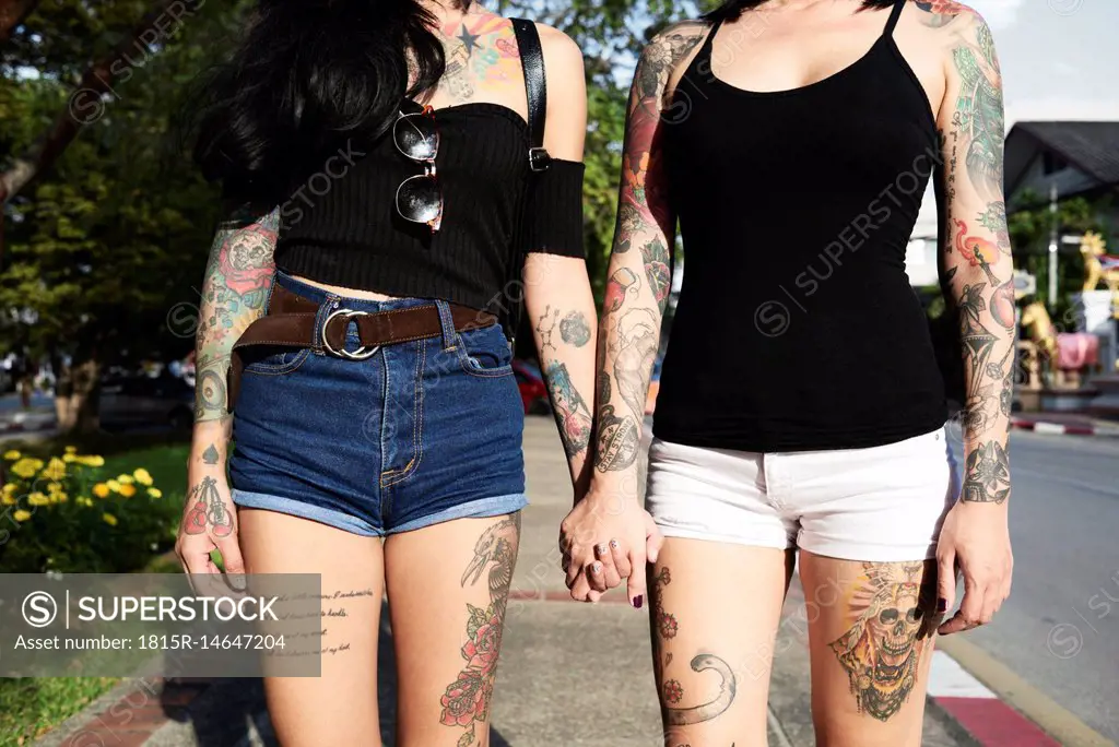 Tattooed lesbian couple holding hands in the street in summer