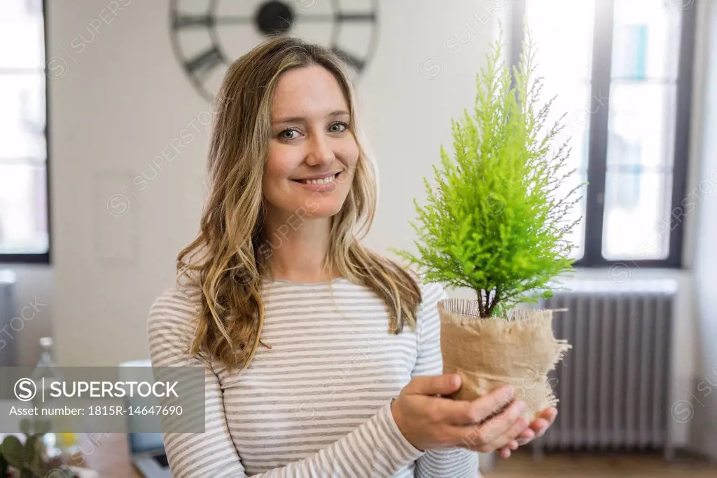 Portrait of smiling woman holding plant at home