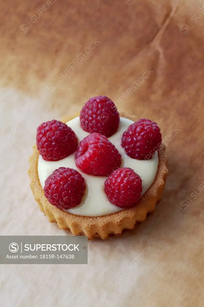 Pie with vanilla pudding and raspberries on baking paper, studio shot