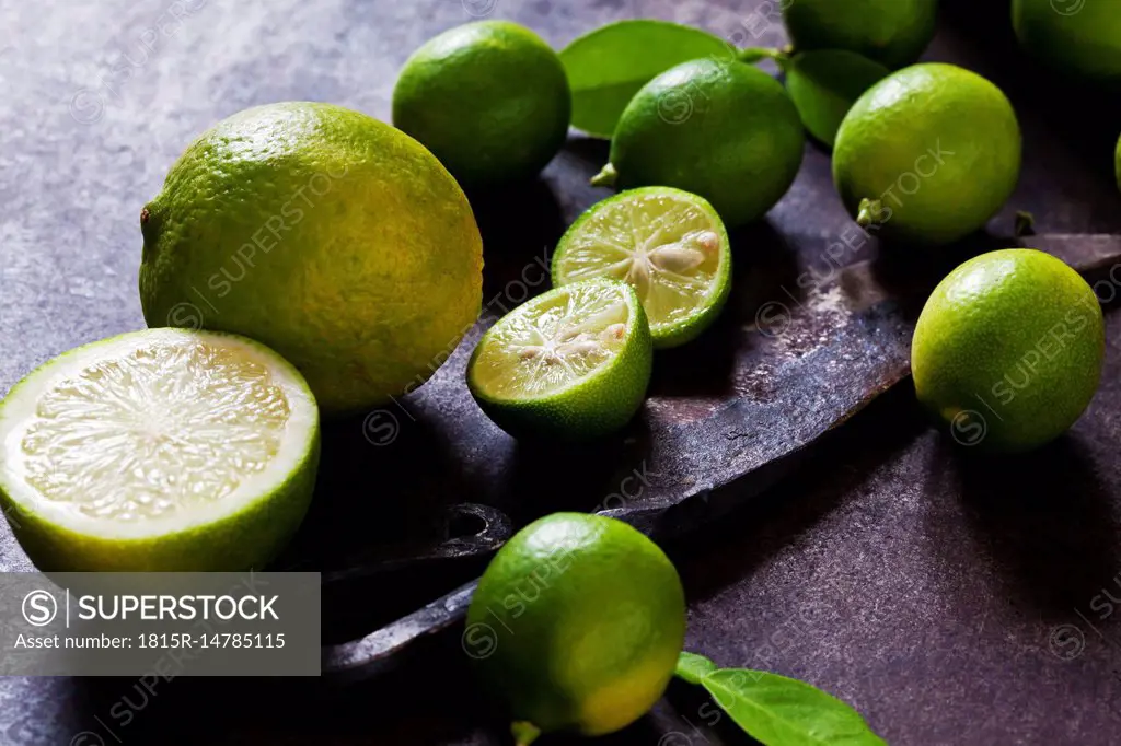 Sliced and whole limequats, limes, leaves and old knife on rusty ground