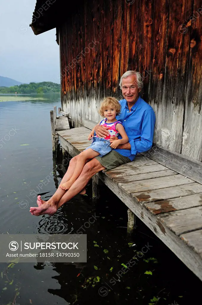 Little girl sitting with grandfather on jetty in summer