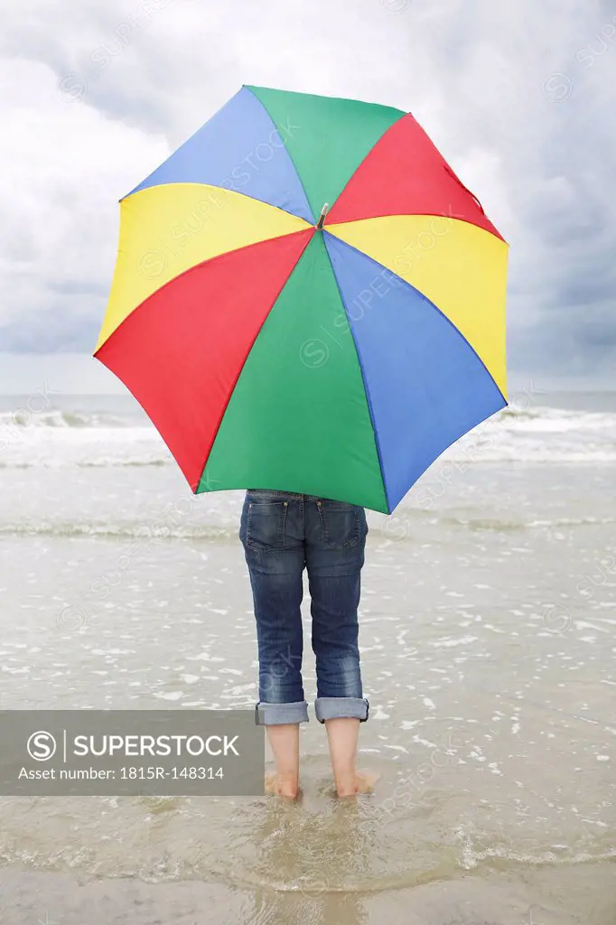 Germany, Lower Saxony, East Frisia, Langeoog, woman with open umbrella standing at the beach