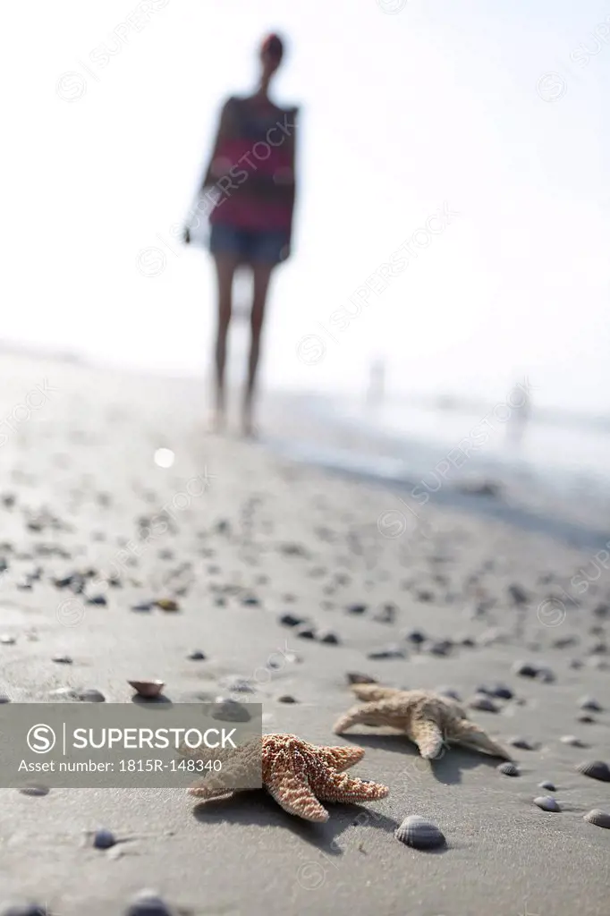 Germany, Lower Saxony, East Frisia, Langeoog, two sea stars and silhouette of a woman at the beach
