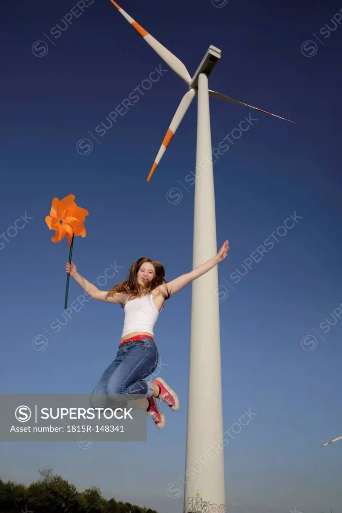 Germany, North Rhine Westphalia, Neuss, female teenager at wind farm jumping in the air with windmill in her hand
