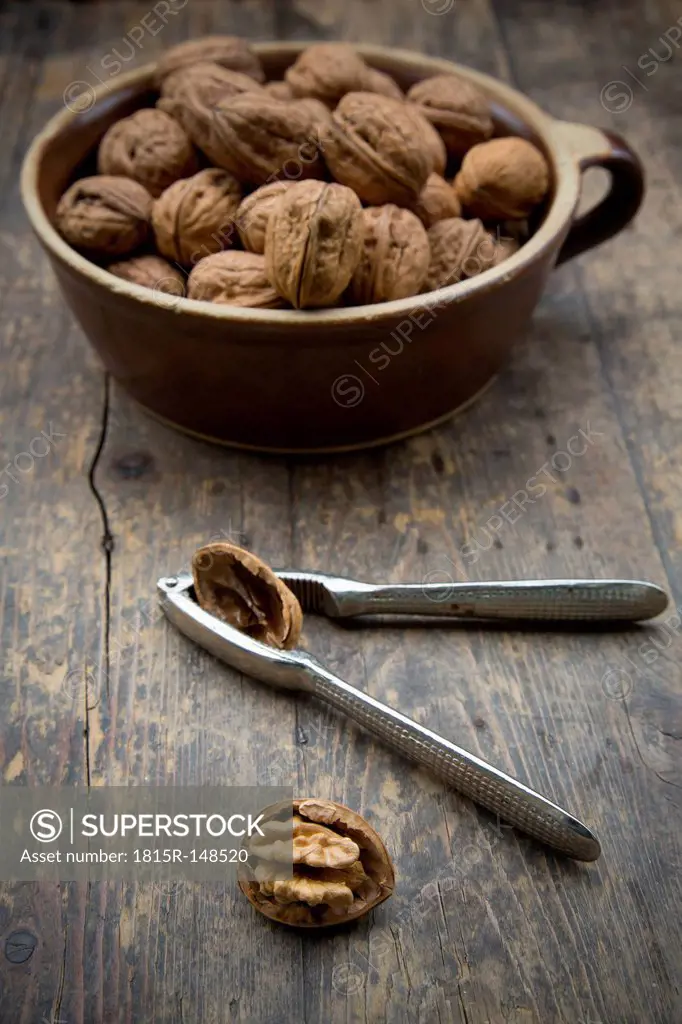 Earthenware bowl with walnuts (Juglans regia) and nutcracker on wooden table, studio shot