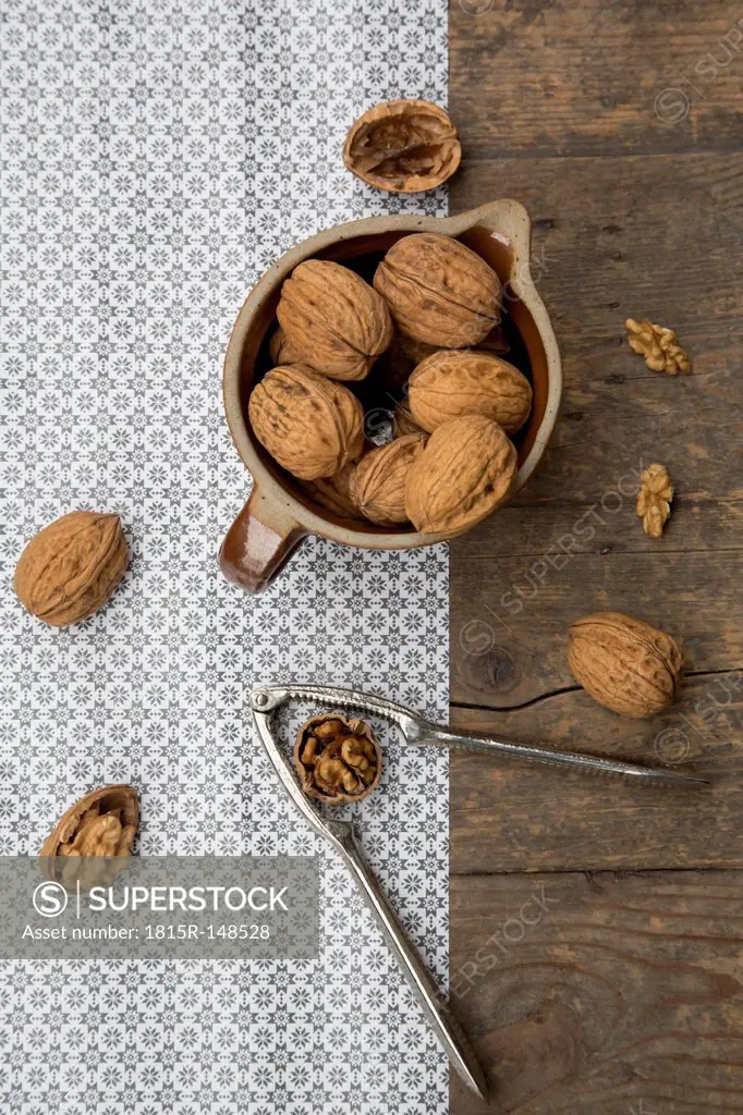 Earthenware jar with walnuts (Juglans regia) and nutcracker on wooden table, studio shot