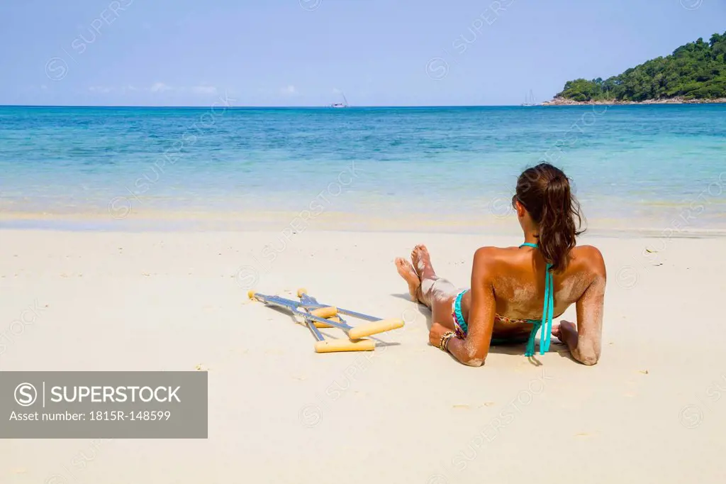 Thailand, Koh Surin island, woman with crutches lying at the white sandy beach