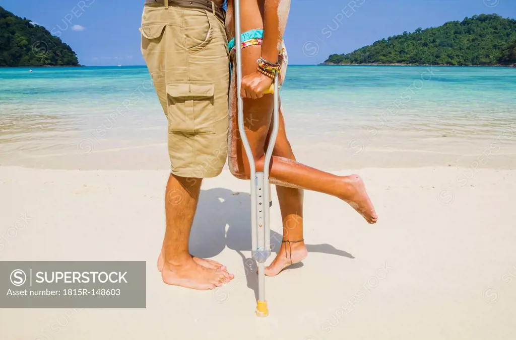 Thailand, Koh Surin island, woman with crutches kissing man at the white sandy beach